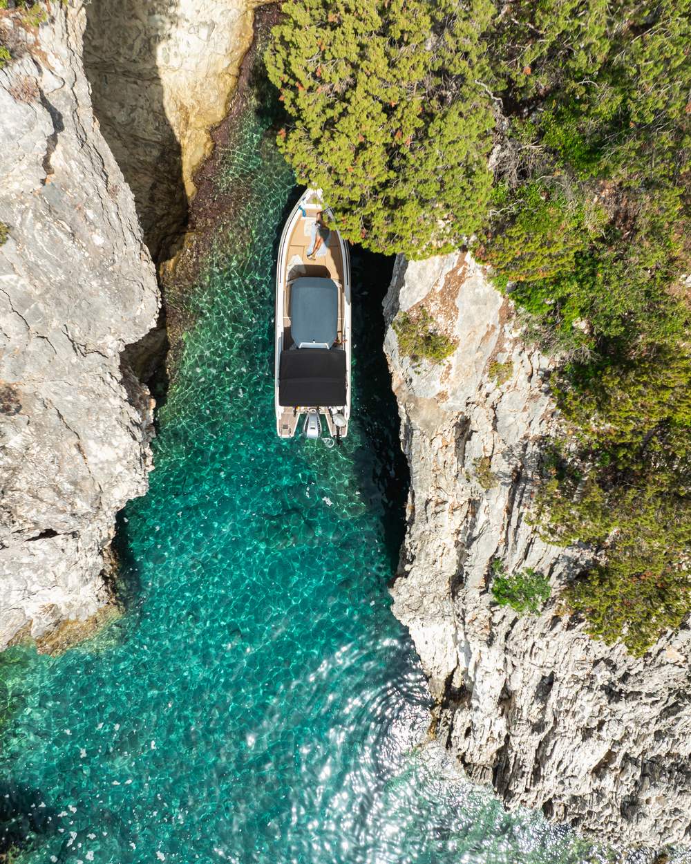 Drone photo of a boat slipping between white cliffs into a turquoise cove in Lefkada