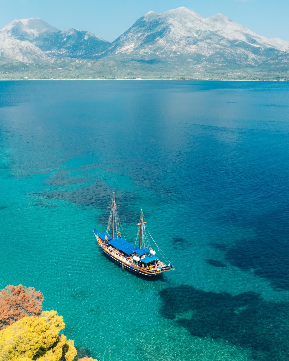 Traditional wooden day-cruise boat on blue water with mountains behind, Ionian sea
