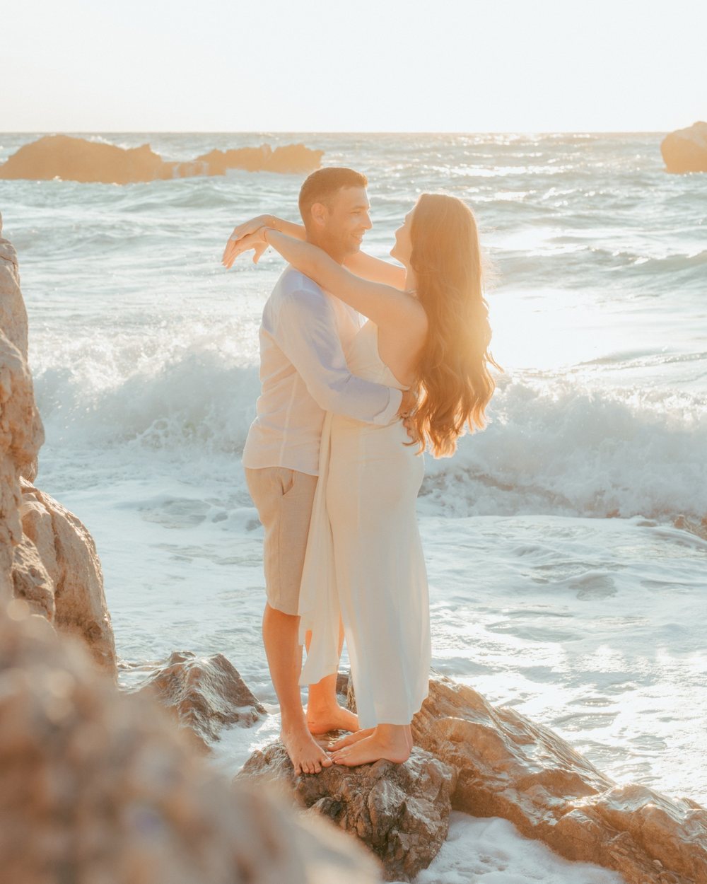Couple embracing on the rocks as waves break, sunset session in Lefkada
