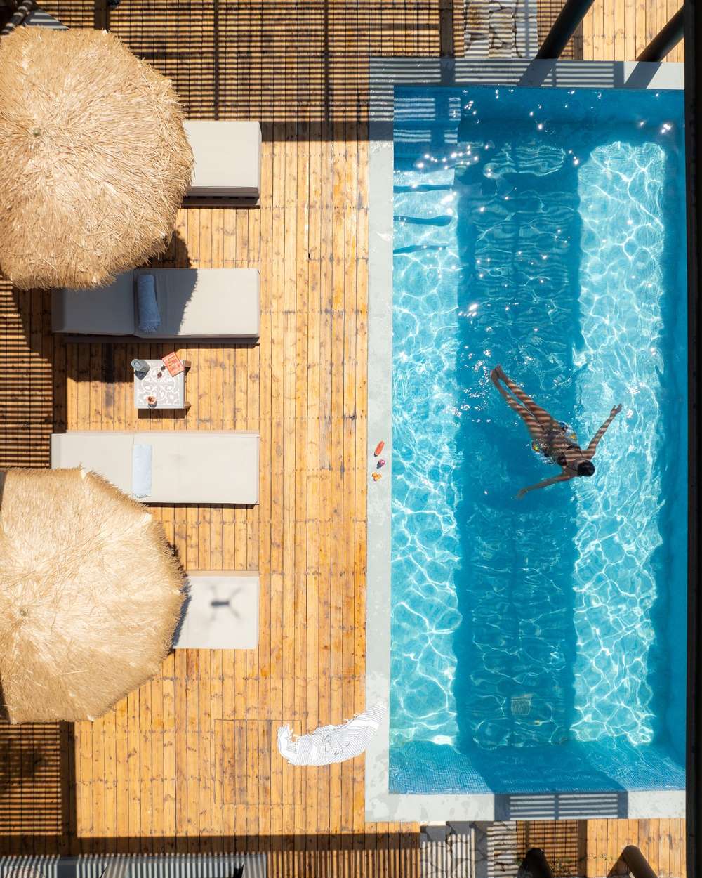 Drone photo of a villa pool with a swimmer and straw umbrellas in Lefkada